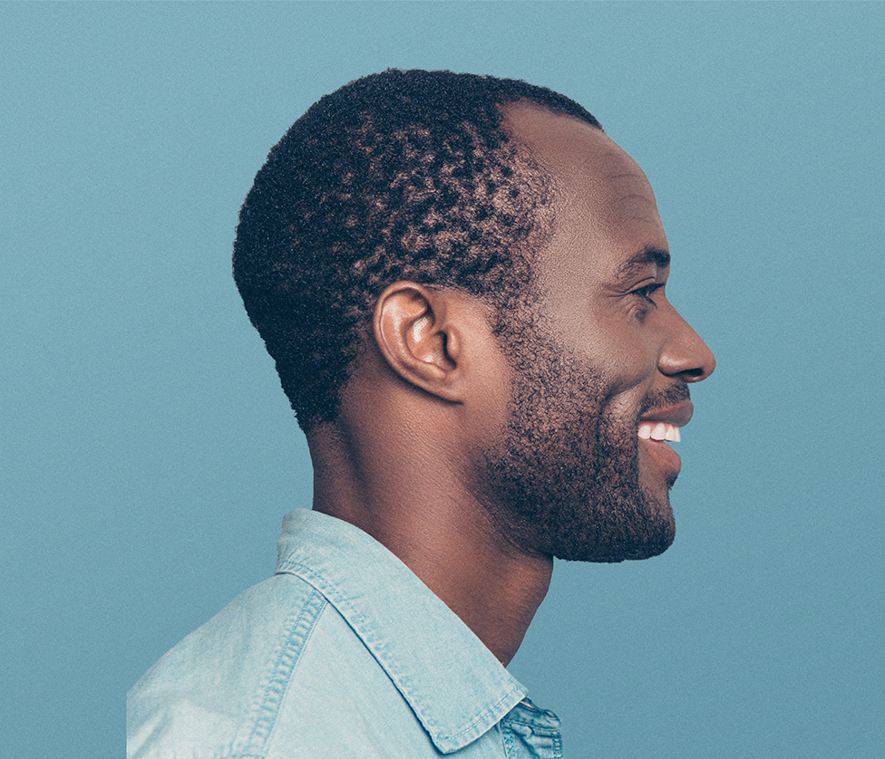 A smiling middle-aged Black man, looking to the right toward a Black female doctor